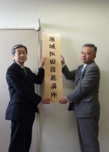 表示板を掲げる上田医学部長（左）と小竹健康福祉部長（右）